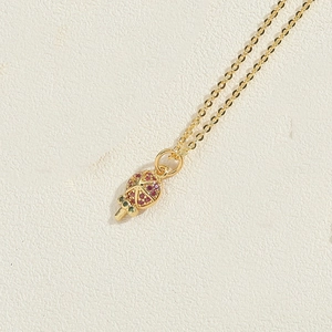 Close-up of gold-plated pomegranate pendant with red and green zircons on chain