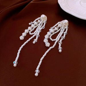 Detail view of long tassel earrings with white pearls and faceted crystal beads on brown fabric