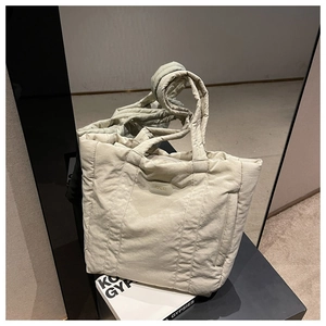 Detail of beige quilted nylon tote bag featuring soft padded texture and dual handles