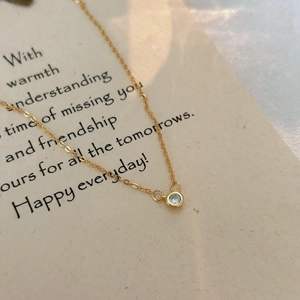 Close-up of a minimalist gold necklace with a single round bezel-set zircon pendant