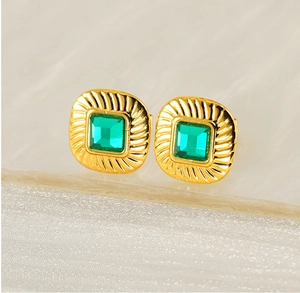 Macro shot of vintage gold square earrings with emerald green zircon and radial texture