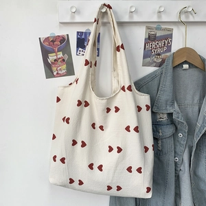 Detail of canvas tote bag featuring red heart patterns and wide shoulder straps