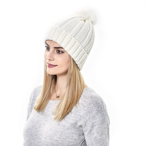 Close-up of a white knit beanie featuring a large faux fur pompom and wide ribbed cuff