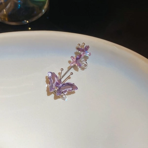 Macro shot of silver butterfly ear cuffs with sparkling purple zircons on white ceramic