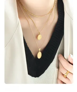 Detail of layered gold titanium steel necklace with coin and oval pendants on a model