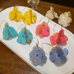 Vue à plat de boucles d'oreilles fleurs en tissu colorées en jaune, blanc, rose et bleu sur plateau
