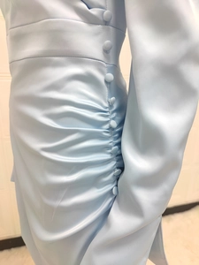 Close-up of light blue satin dress featuring waist button detail and elegant pleats