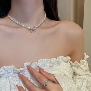 Close-up of elegant double-layered pearl necklace with diamond bow pendant and silver ring