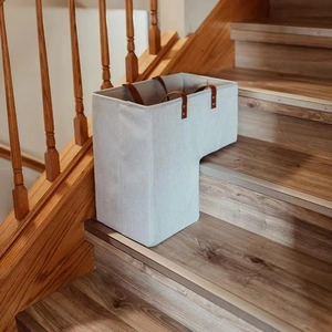 Grey L-shaped fabric stair basket with brown leather handles on wooden steps