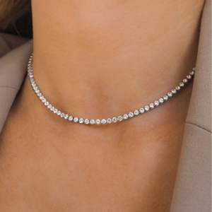 Close-up of a silver single-row tennis necklace with sparkling round crystals on a model