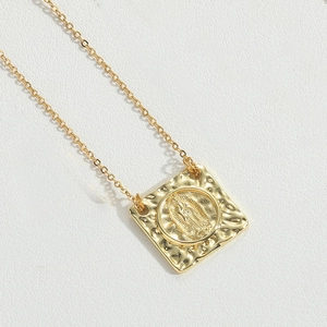 Detailed close-up of golden square Virgin Mary pendant on white textured leather background
