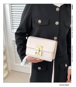 Detail of a cream rectangular flap bag with a glossy finish and a golden geometric buckle