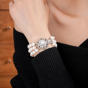Macro detail of triple-layer pearl bracelet with silver floral clasp on model wrist