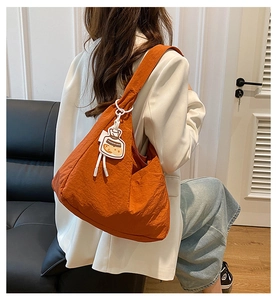 Model wearing a large orange canvas tote bag with a cartoon charm on the shoulder