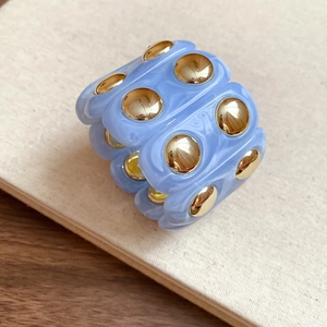 Macro shot of sky blue resin band ring with golden metallic rivets on wooden surface