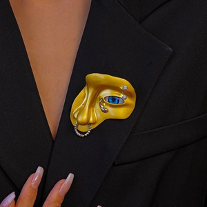 Broche visage artistique avec anneau de nez et oeil bleu sur revers de veste sombre