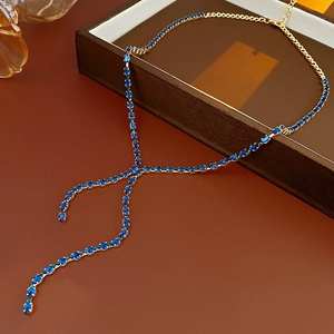 Detailed view of gold Y-shaped necklace with blue zircon teardrop pendant on wood surface