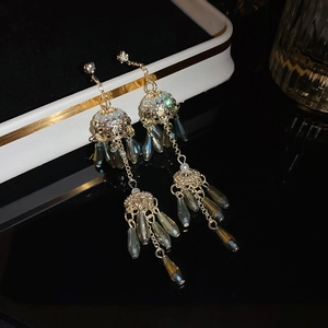 Close-up of bohemian gold tassel earrings with grey crystal beads on black surface
