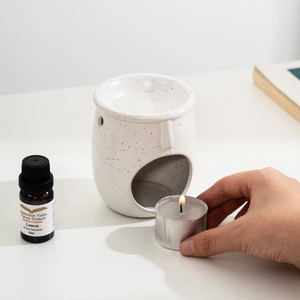 Placing a lit tea light candle into a white ceramic face-shaped essential oil burner