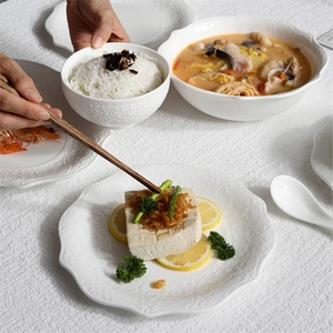 Elegant white embossed ceramic tableware set featuring dinner plates and bowls in a home setting