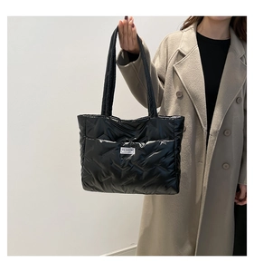 Detailed view of the large black quilted tote bag worn with a stylish beige coat
