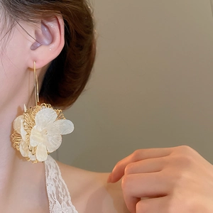 Gros plan d'une boucle d'oreille fleurie dorée et blanche portée par un mannequin