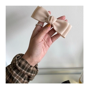 Detail shot of a beige satin bow hair clip held in hand showing smooth fabric texture