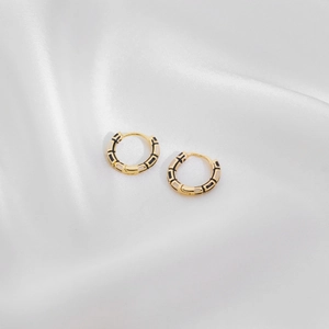 Detailed macro view of gold-plated hoop earrings with black and white enamel pattern
