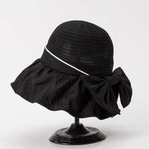 Close-up of black hollow sun hat with ribbon bow and elegant brand logo pattern