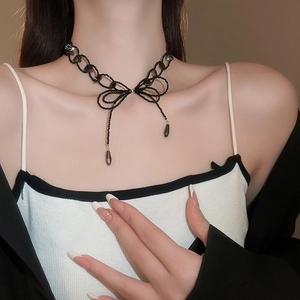 Detail of elegant black beaded bow necklace with teardrop charms on model neck