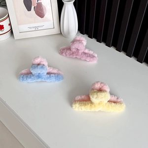 Three plush faux fur hair claws in pink, blue, and yellow on a clean white surface