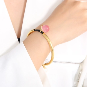Detailed close-up of gold titanium bangle featuring pink beads and black braided rope accent