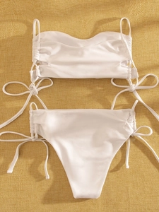 Detailed flat lay of white bikini set with side drawstrings on beige textured fabric