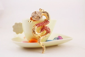 Macro detail of gold snake pendant with pink and clear crystals on a tea cup