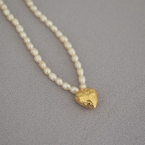 Close-up of freshwater pearl necklace featuring a textured golden heart-shaped coin pendant