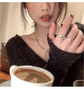 Close-up of stacked silver heart rings and pearl necklace worn in a cozy cafe setting