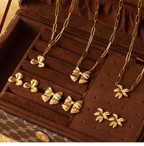 Detailed set of gold bow and flower necklaces with paperclip chains in a velvet box