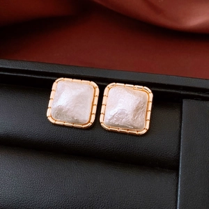 Macro shot of square gold earrings with white textured resin inlays on a black display