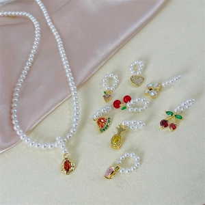 Close-up of pearl necklace with fruit charms like cherry and grape on silk fabric