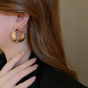Close-up of chunky gold double-layered hoop earrings worn by a model in a minimalist style