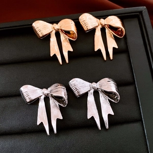 Close-up of bow-shaped stud earrings in silver and rose gold on black leather tray