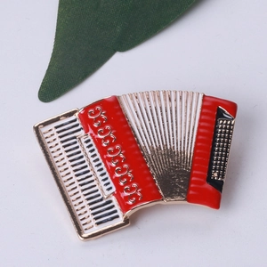 Flat lay of a red and gold enamel accordion brooch on a white surface with a green leaf