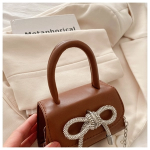 Detail of a brown leather mini bag with a sparkling rhinestone bow and chain strap