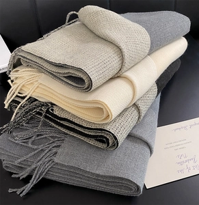 Close-up of stacked winter scarves with soft fringe details in grey and beige tones