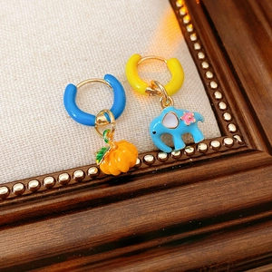 Macro view of asymmetric enamel earrings featuring a blue elephant and orange pumpkin charm