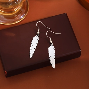 Close-up of silver feather drop earrings with intricate texture on a premium jewelry box