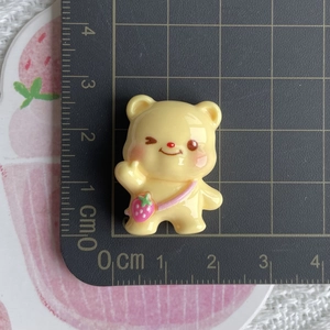Macro shot of yellow resin bear charm with strawberry bag on a cm scale cutting mat
