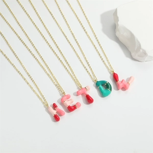 Detail of gold necklaces with colorful rounded enamel letter pendants on a white stone