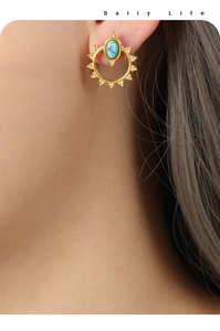 Close-up of golden sunburst earrings with natural turquoise stone on model ear