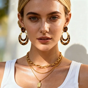 Detail of a woman wearing gold hoop earrings with leopard print and layered necklaces